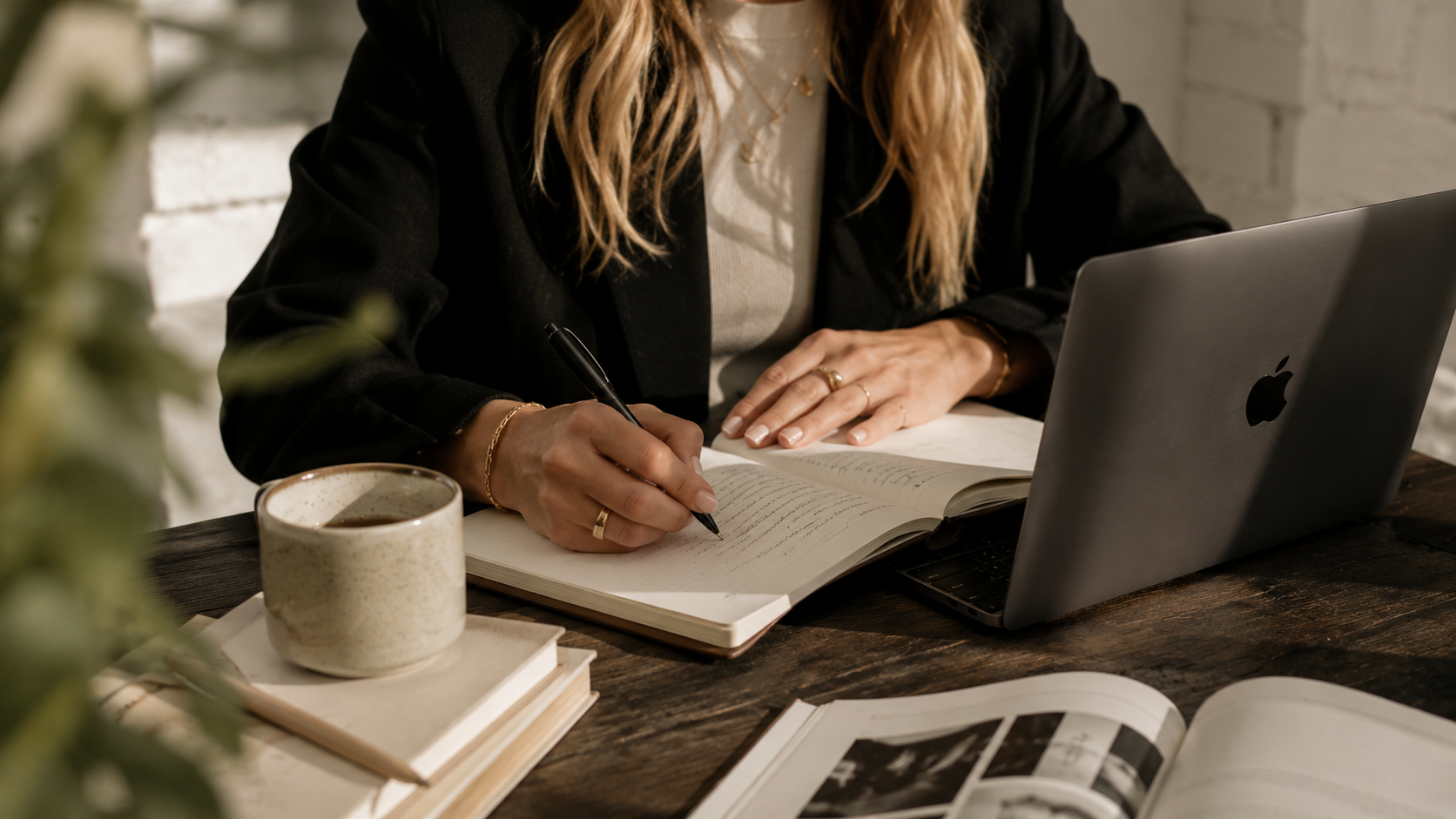 An editor typing on a laptop at a warm-lit desk, coffee and a red pen alongside a notebook